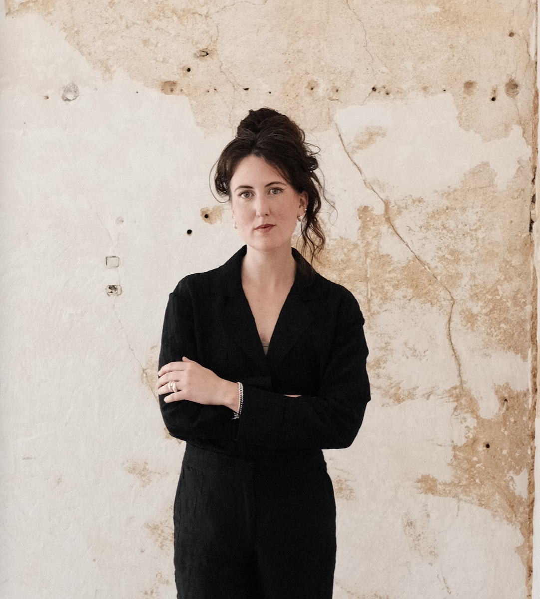 Emma G. Möller, arms folded, in front of a plaster wall